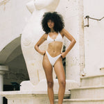 Woman in a white bikini standing on stone steps with a decorative wall in the background