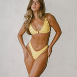 Woman wearing a yellow bikini against a plain background