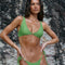 Woman wearing a green bikini standing against a rocky background