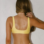 Woman wearing a yellow bikini standing against a plain wall.
