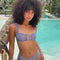Woman in a checkered bikini standing by a pool with palm trees in the background