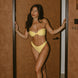 Woman in a yellow bikini standing in a doorway with a warm-toned wall and number 1405 visible.
