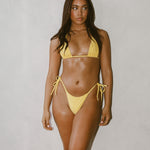 Woman wearing a yellow bikini standing against a plain background