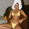 Woman in yellow bikini sitting on a couch with a towel on her head, holding a drink.